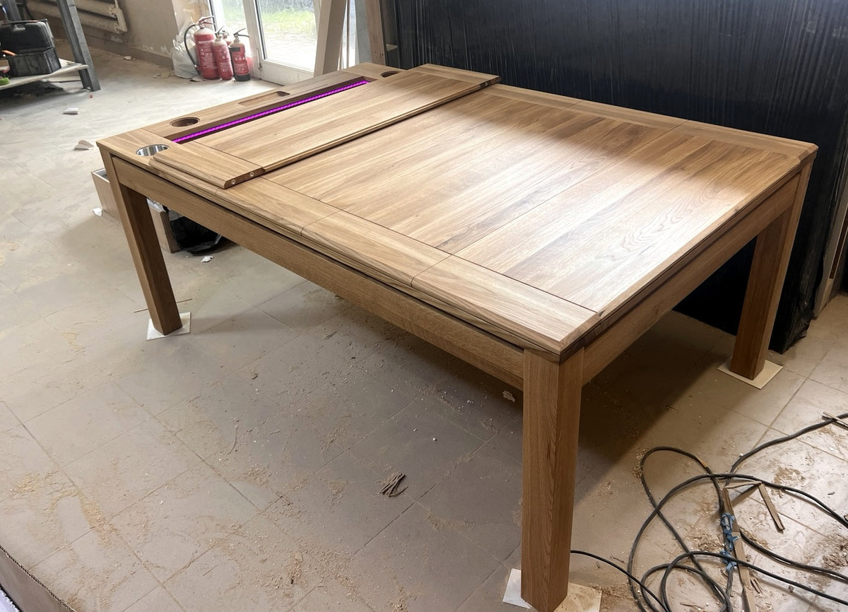 Solid oak Sojourn game table with partially open dining top and pink LED lighting, photographed in the workshop